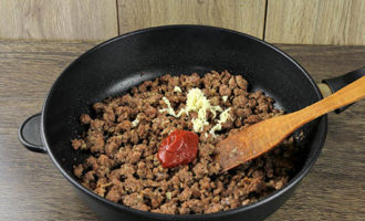Tillsätt hackad vitlök och tomatpuré i köttfärsen, lite kokande vatten och låt puttra tillsammans i minst 7-10 minuter.