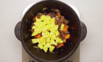 Vid det här laget ska grönsakerna redan vara skalade och tvättade. Skär löken och morötterna i halva ringar, lägg dem i köttet och fräs allt tillsammans under omrörning. Lägg sedan till potatisen, skuren i små tärningar, i behållaren och stek allt tillsammans. Sänk värmen för att förhindra att grönsaker och kött bränns fast.