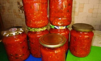 Turnați adjika clocotită în borcanele pregătite și acoperiți cu capace. Luați o cratiță foarte mare, puneți în ea borcane cu preparate vegetale, turnați apă în cratiță astfel încât să acopere aproape complet borcanele (ar trebui să rămână 1-2 degete până la vârful borcanului). Aduceți apa la fiert și lăsați borcanele de adjika să fiarbă aproximativ 15 minute, apoi îndepărtați cu grijă borcanele fierbinți și sigilați-le imediat cu capace. Întoarceți piesele cu susul în jos și acoperiți cu o pătură caldă. După ce s-au răcit complet, mutați borcanele într-un loc în care va fi în mod constant întuneric și răcoros.