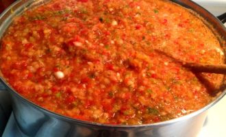 Se toarnă masa de legume rezultată într-o cratiță destul de spațioasă, se adaugă zahăr, sare, ulei de floarea soarelui, oțet și se pune la foc mediu. După ce adjika fierbe, reduceți focul și fierbeți timp de aproximativ 20 de minute.În timp ce adjika se gătește, spălați borcanele în apă fierbinte cu o cantitate mică de bicarbonat de sodiu adăugat. 