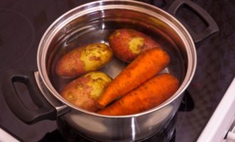 Cum să gătești hering sub o haină de blană cu un ou conform rețetei clasice? Deoarece salata este preparată din legume fierte, primul lucru pe care trebuie să-l faceți este să le pregătiți. Așadar, clătiți bine cartofii și morcovii sub jet de apă. Puneți-le într-o cratiță și adăugați suficientă apă. Când legumele ajung la fiert, reduceți focul și fierbeți până când pot fi străpunse ușor cu o furculiță (dar atenție, legumele se gătesc foarte ușor și vor începe să se destrame). După ce legumele sunt gata, trebuie să le transferați pe o farfurie largă pentru a se răci. Pune ouăle de pui într-o altă tigaie, se pun pe foc și se fierb după fierbere 8-10 minute. După ce a trecut timpul, scurgeți apa clocotită din ouă și adăugați apă rece pentru a ajuta la curățarea mai bine a cojilor.