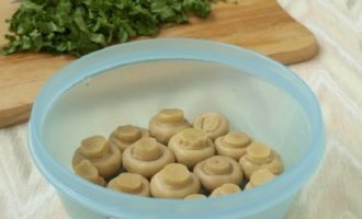 Forma de asamblare a salatei poate fi acoperită cu folie alimentară sau ușor unsă cu ulei vegetal, apoi puneți șampioanele acolo, capacele în jos.