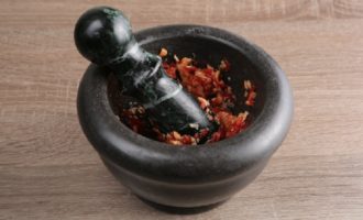 Talleu el xile per la meitat, traieu les llavors i les membranes de dins. Piqueu finament el xile i els alls pelats i després tritureu-los en un morter, afegint-hi una mica de sal.