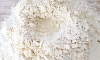 Tạo một lỗ trên gò từ những mảnh vụn đã chuẩn bị sẵn và đổ hỗn hợp trứng và nước vào đó từng phần (từng chút một), đồng thời dùng tay gom khối bột thu được thành một cục. Đừng nhào bột mà chỉ vo thành một cục lớn.