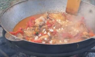 După aceasta, adăugați roșiile și pasta de roșii, amestecați bine pentru a combina toate ingredientele și fierbeți timp de 5-7 minute. Apoi adăugați ardei gras, aduceți vasul la fierbere activ, apoi adăugați usturoi, ierburi, condimente și sare, amestecați.