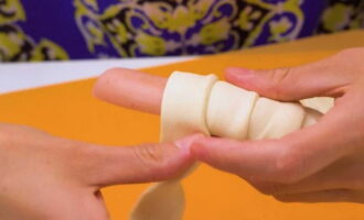 Învelim fiecare cârnați cu fâșii de aluat astfel încât fiecare tură ulterioară să se suprapună pe cea anterioară. 