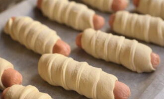Pregătiți o foaie de copt - acoperiți-o cu pergament. Puneți cârnații în aluat acolo.