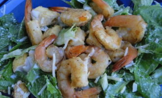 Într-un vas separat, combinați salata verde, creveții și crutoanele. Adaugă aici dressingul și amestecă cu două linguri, având grijă să nu piurezi verdeața și creveții. Presărați salata cu brânză rasă.