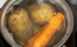 Om Mimosa-salade met ingeblikte vis volgens het klassieke recept te bereiden, bereidt u alle ingrediënten voor. Was de aardappelen en wortels, doe ze in een pan, bedek ze met water en kook tot ze gaar zijn.
