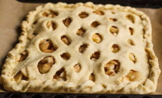 Pagulungin sa isang layer na humigit-kumulang sa parehong lapad, ngunit medyo mas makitid, ang kuwarta para sa tuktok ng pie.Nag-iiwan kami ng mga hiwa sa isang pattern ng checkerboard at iunat ang kuwarta nang malawak. Ilagay ang tuktok sa ibabaw ng pagpuno at i-seal ang mga gilid.