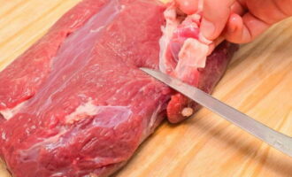Het door ons gekozen vlees maken we schoon van de witte folie. Van 150 gram rundvlees krijgen we twee porties carpaccio. Voor één portie is ongeveer 70 gram vlees nodig. De bereide ossenhaas moet strak in huishoudfolie worden gewikkeld.We stoppen het vlees in de vriezer. Dankzij dit kunnen we het gemakkelijk snijden. Afhankelijk van de grootte van de ossenhaas en de vorm zal het vlees 1,5 tot 2 uur invriezen.  