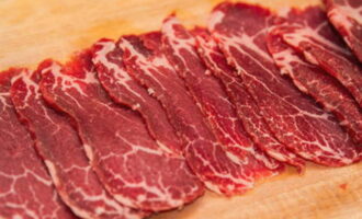 Wanneer het vlees enigszins bevroren is, haalt u het uit de vriezer. Snijd de filet in kleine en dunne plakjes. Hun dikte moet ongeveer 2 millimeter zijn. Voor het snijden nemen we het scherpste mes. Als alle messen in je keuken bot zijn, is het de moeite waard om de tijd te nemen om ze te slijpen. In dit geval zullen de plakjes erg dun en bijna transparant zijn. Misschien heb je een snijmachine in je keuken. Dan kunt u het gebruiken en tijd besparen. Als u meerdere porties gaat bereiden, is het handig om de resulterende plakjes op huishoudfolie te leggen. Het moet op een vlakke ondergrond liggen, bijvoorbeeld op een tafel. We leggen de plakjes in verschillende lagen. Bedek elke laag met huishoudfolie. Vervolgens leggen we de plakjes in de vriezer totdat ze worden geserveerd. Wees niet bang dat ze te veel bevriezen. Plakjes ontdooien zeer snel bij kamertemperatuur.  