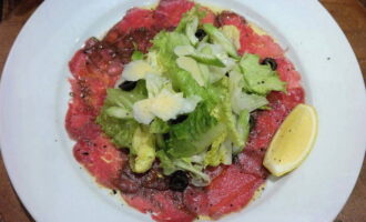 Haal de vleesplakken uit de vriezer. Leg ze in een gelijkmatige laag op een bord. We moeten de carpaccio bestrijken met dressing. Voor het gemak kunt u een deegborstel gebruiken. Met zijn hulp verdelen we de dressing gelijkmatig over elk stuk, waardoor ze goed worden bevochtigd. Dan kan de carpaccio goed marineren. Bestrooi de plakjes voor het serveren met gemalen amandelen en stukjes zongedroogde tomaat. Meng slablaadjes met de rest van onze dressing. Leg ze op het vlees en voeg vervolgens Parmezaanse kaas toe. Het gerecht moet snel geserveerd worden. Laat het niet opwarmen tot kamertemperatuur. Het gerecht is klaar en je kunt je gasten verrassen met zo'n voortreffelijk en smakelijk voorgerecht.    