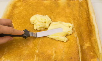 A kihűlt kekszet óvatosan csomagoljuk ki. Néhol megreped, ez normális, a lényeg, hogy ne essen szét teljesen. Vágja le a végeit egy késsel, és tegye félre a szegélyeket. A kekszet cukorszirupba áztatjuk, és 10 percig pihentetjük. Ezután hozzáadjuk a színtelen krémet, és egyenletes rétegben elkenjük vele a tortát.