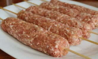 Les mans s'han de mullar amb aigua. Agafeu una petita quantitat de carn picada i feu-ne una bola. Ho aplanem en un pastís pla. Ara hem d'enganxar amb molta cura la carn picada al voltant de la broqueta. Com a resultat, obteniu una costella oblonga. 
