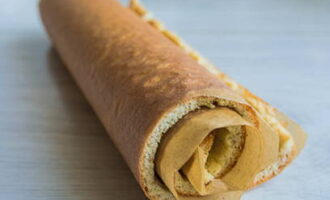 Ha kész a piskóta, vegyük ki a sütőből, és tegyük át egy új sütőlapra. Távolítsa el a régi pergament, ügyelve arra, hogy ne sértse meg a tortát, majd tekerje fel a réteget egy második sütőpapírral együtt, és hagyja kihűlni.