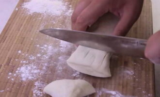 Cand aluatul s-a asezat il scoatem din recipient. Pudrați o scândură de lemn cu făină. Tăiați aluatul în bucăți mici.Mărimea lor poate varia în funcție de dorința dvs. Rețineți că, pe măsură ce coaceți plăcintele, acestea vor crește în dimensiune. 