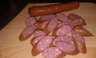 Hoe eenvoudig en heerlijk pasta met worst koken? Neem je favoriete worstjes mee of de worstjes die nog in de koelkast liggen. Het is het beste om jachtworsten in dit gerecht te gebruiken; deze voegen een speciale rokerige smaak en geur toe. Snijd ze op een snijplank in langwerpige cirkels.