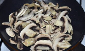 Poseu els bolets en un recipient profund i ompliu-los d'aigua. Rentem els xampinyons diverses vegades, escorrem l'aigua i els col·loquem sobre paper absorbent per absorbir l'excés d'humitat. Col·loqueu la paella al foc. Ompliu-lo amb aigua freda i afegiu-hi els bolets. No cal cuinar-los durant molt de temps. Espereu uns 5-7 minuts i apagueu el foc. Talleu els bolets a trossos petits. Posar la paella al foc i untar-la amb oli vegetal. Fregiu els bolets durant 10 minuts. Com a resultat, la vostra cuina s'ha d'omplir d'una aroma rica.  