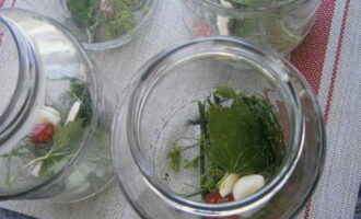 Doe de gepelde knoflookteentjes, chilipepers, mierikswortelwortel, dilleparaplu, mosterd en kersenblad in een gesteriliseerde pot.