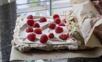 Nadat de meringue is afgekoeld, smeert u een laagje room en legt u de frambozen neer. We laten een paar centimeter vrij aan één rand en beginnen de rol in te pakken. Tijdens het walsproces zal de meringue een beetje breken, wat je niet hoeft te laten schrikken.