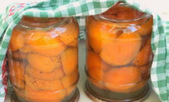 Giet de siroop over de abrikozen en rol de pot op. We bedekken het met een deken of deken, dat wil zeggen, we creëren omstandigheden voor een stoombad: op deze manier zal de compote een nieuwe sterilisatiefase ondergaan en beter worden bewaard. Het beste kunt u de compote op een koele plaats bewaren, met een temperatuur niet hoger dan 18 graden. Het kan ongeveer een jaar blijven staan. 