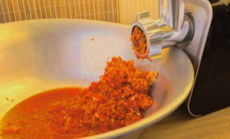 Hur förbereder man adjika enligt det klassiska receptet för vintern? Vi tvättar den nödvändiga mängden tomater, chilipeppar och paprika i varmt vatten. För att inte vänta länge på att fukten ska rinna av, blötlägger vi dem med en handduk. Använd en vass kniv och skär ut alla onödiga delar av grönsakerna: kärnan och svansarna på paprikan, stjälkarna och platser där de är fästa på tomaterna. Skär paprikan och tomaterna i bitar och lägg dem i en köttkvarn. Mal till massa. 
