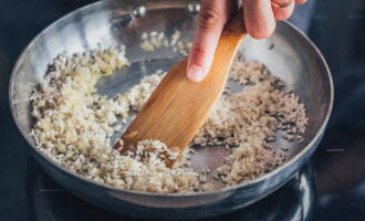 Matapos lumitaw ang katangian ng amoy ng bawang, alisin ang durog na sibuyas. Ibuhos ang natitirang mantika at magdagdag ng bigas. Init ito sa isang kawali, patuloy na pagpapakilos gamit ang isang spatula.