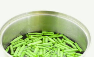 Cum se prepară un preparat simplu de fasole verde pentru iarnă? Spălați fasolea, tăiați cozile pe ambele părți și tăiați păstăile în bucăți lungi de 2-2,5 centimetri. Se fierbe apa intr-o cratita, se pune fasolea in ea si se fierbe 10 minute dupa fierbere.