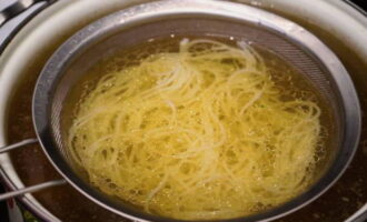 Låt oss börja montera skålen. Lägg nudlarna i ett durkslag och värm dem i nötbuljong, lägg dem sedan på botten av en djup skål, toppad med hackat kokt kött, vitlökrötter, chilipepparringar, böngroddar och färska örtblad. 