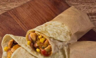 Nu kan du gå vidare till att montera burritos. Lägg 3-4 matskedar fyllning på tortillas. Vik först in nederkanten, sedan sidorna. Slå in burritons underkant i pergament eller folie för att förhindra att fyllningen läcker ut.