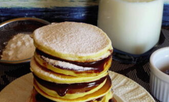 Leg vervolgens een eetlepel chocolade op de pannenkoek, bedek met de tweede pannenkoek en bestrooi met poedersuiker. Een heerlijk dessert is klaar.