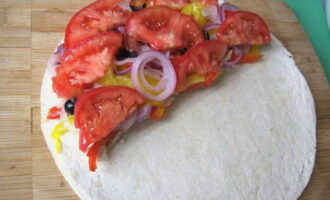 Voeg vervolgens de uien, olijfringen en tomatenblokjes toe. De tortilla wordt zorgvuldig dubbelgevouwen. 