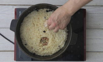 Als de rijst al het vocht heeft opgenomen, druk je er twee knoflookteentjes in (slechts halverwege), zet je het vuur laag en laat je de pilaf onder een gesloten deksel sudderen.