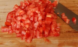 Vi tvättar tomaterna och blir av med skalet: vi skär snitt på toppen av tomaterna i form av ett kors och skållar tomaterna med kokande vatten, efter ett par minuter kommer skalet lätt att lossna från fruktköttet. frukt. Skär tomaterna i tärningar (ta bort kärnorna). 