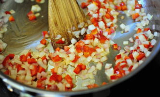 Col·loqueu les costelles cuites de la paella en un plat. Rentar el pebrot i treure-li la tija amb un ganivet. A continuació, talleu la fruita per la meitat per treure el nucli. Talleu el pebrot i la ceba prèviament pelada a daus petits. Poseu les verdures a la paella amb la resta d'oli i greix de porc. Sofregiu-los durant 10 minuts fins que estiguin toves.