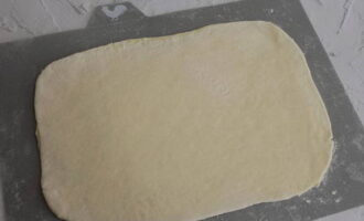 Rol de laag gistdeeg uit tot een grote platte cake, rekening houdend met de grootte van de bakplaat.