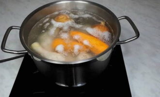 Was de ui goed en doe deze bij de kip in de pan. Leg vervolgens de geschilde wortels daar, giet er ongeveer 1,5 liter water bij, zet het op het vuur, breng de bouillon aan de kook en verwijder het resulterende schuim.