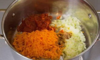 Wanneer de ui glazig wordt, voeg je geraspte wortels, tomatenpuree en aromatische kruiden toe, meng en kook ongeveer 5 minuten.
