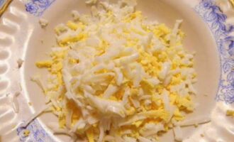 Grate ang mga pinalamig na itlog sa isang magaspang na kudkuran at ilagay sa isang karaniwang mangkok kasama ng mga crab stick.