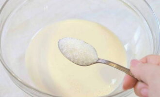 Om luchtige pannenkoeken met gefermenteerde gebakken melk te bereiden, verwarmt u deze lichtjes en giet u deze in een kom. Voeg suiker en zout toe. Meng de ingrediënten goed.