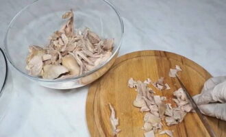 We halen de ui uit de bouillon en gooien hem weg. Doe de kip in een diepe bak, laat hem afkoelen, haal het vlees van het bot en snijd het in kleine stukjes.