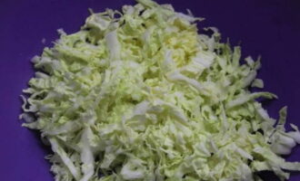 Hoe maak je een eenvoudige en smakelijke salade met champignons klaar? Snijd de Pekingkool fijn en doe ze in een diepe kom.