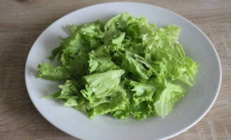 Hoe maak je een heerlijke forelsalade klaar? We wassen de slablaadjes, drogen ze, scheuren ze met onze handen in stukjes en leggen ze op een bord.