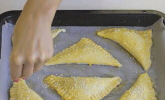 Preescalfeu el forn (ajusteu la temperatura a 200 graus). Folreu el fons d'una safata de forn amb paper de forn. Distribuïu els pastissos. Col·loqueu la safata de forn amb els preparats a la nevera durant 10 minuts. Pinteu els pastissos amb el rovell d'ou restant. Perforar amb una forquilla en diversos llocs. Espolvorear les preparacions amb llavors de sèsam.
