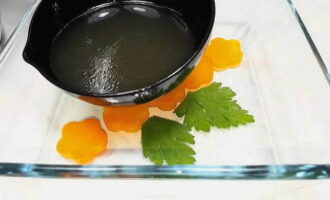 Snijd de gekookte wortels in plakjes en plaats ze in een vorm voor gelei-vlees. Doe dan de peterselie erbij, giet een pollepel gekoelde bouillon en zet het 10-15 minuten in de koelkast. Dit zal de bovenkant van het gelei-vlees zijn.