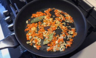 Snijd de tweede helft van de ui en het teentje knoflook fijn. Snijd de wortels in blokjes. Fruit de ui, knoflook en wortels in plantaardige olie tot ze zacht zijn. Voeg het laurierblad toe en kook nog 2 minuten.