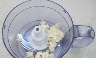 We halen de boter uit de koelkast, bewaren hem 10-15 minuten op normale huistemperatuur, snijden hem vervolgens in kleine stukjes en doen hem in de kom van een keukenmachine met een snijmesopzetstuk.