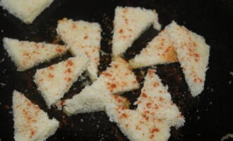 Verdeel het witte brood in kleine stukjes. Bak ze, bestrooid met paprika.