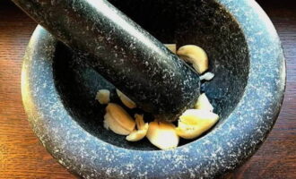 La carn de vedella en màniga al forn és molt fàcil de preparar. Anem a fer la marinada: pelem cinc grans d'all i triturem en un morter o piquem finament.